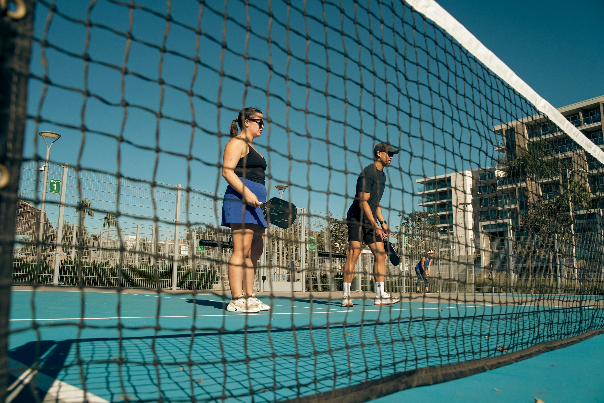 Two doubles partners waiting at the kitchen line, seen low through the net
