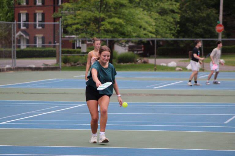 Woman stepping in to hit a low forehand during a recreational doubles game on an outdoor court