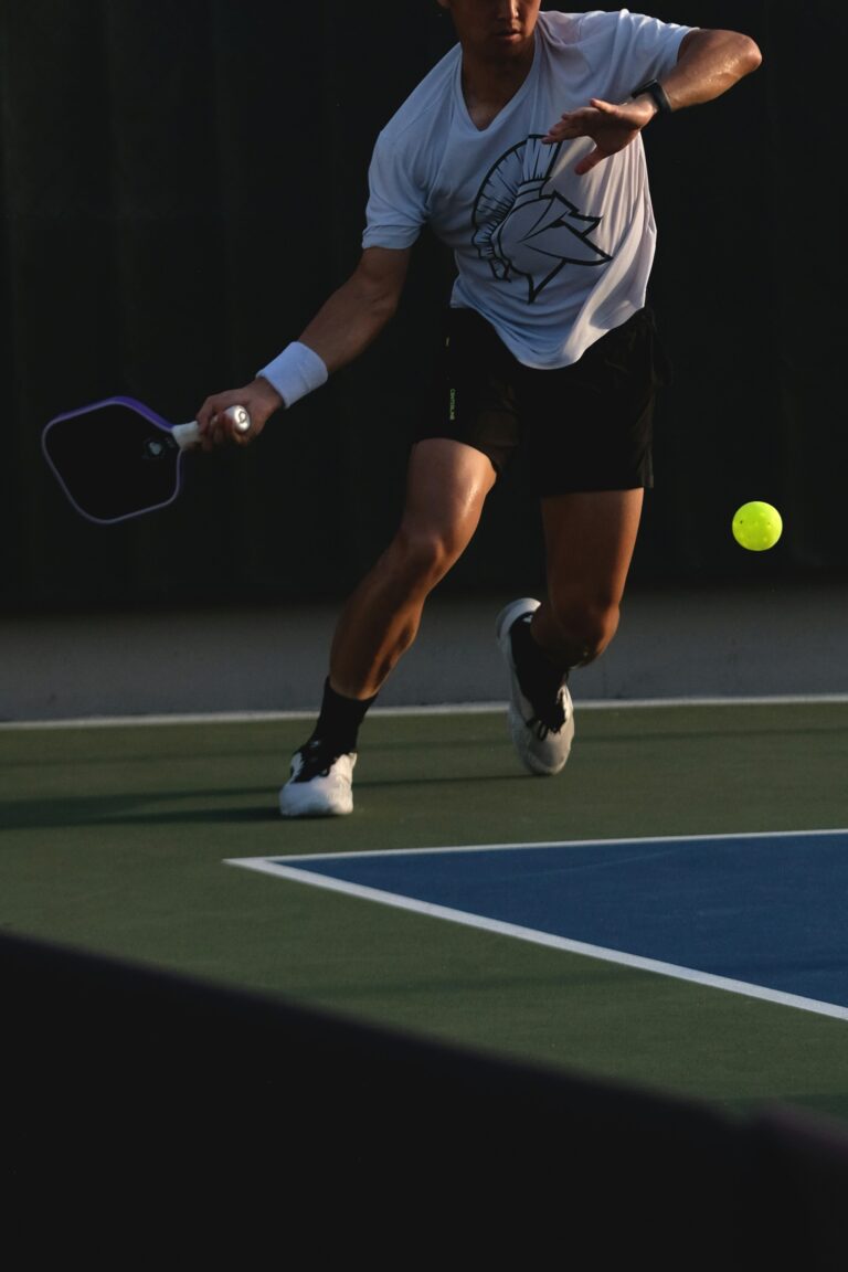 Player lunging forward to reach a low ball near the kitchen line, lit against a dark background