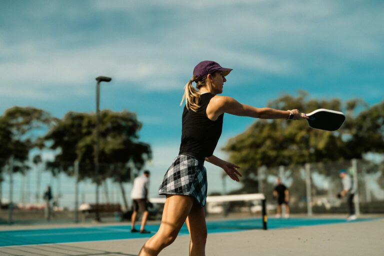 Woman in a cap following through on a forehand drive on a sunny outdoor court
